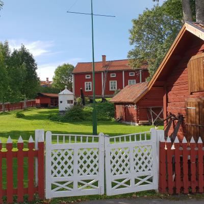 Öregrunds hembygdsgård. Faluröd byggnad med vita knutar. Rött staket med vita grindar. Lada i förgrunden