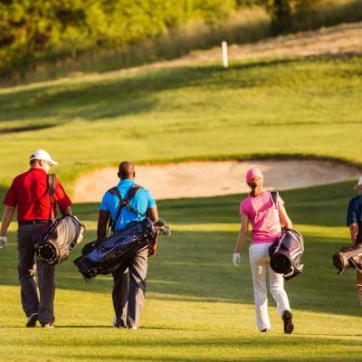 Ryggarna på fyra golfare med färgglada kläder på en grön golfbana