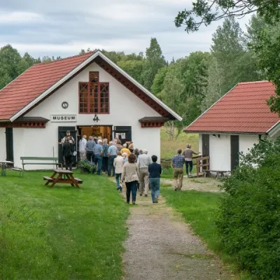 Liten byggnad med vit puts och rött tegeltak och orde Museum på väggen. Köande människor utanför.