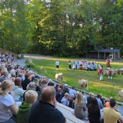 Utomhus teater med en stor publik i förgrunden och skådespelare i bakgrunden