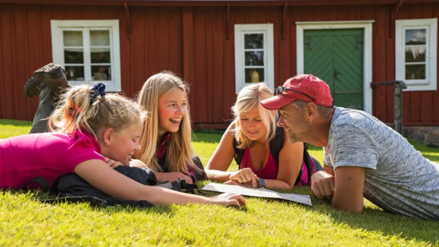 Familj som ligger i gräset och tittar på en ledkarta