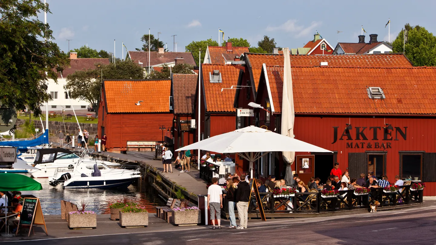 Skärgårdskrog i röda båthus med uteservering och båthamn