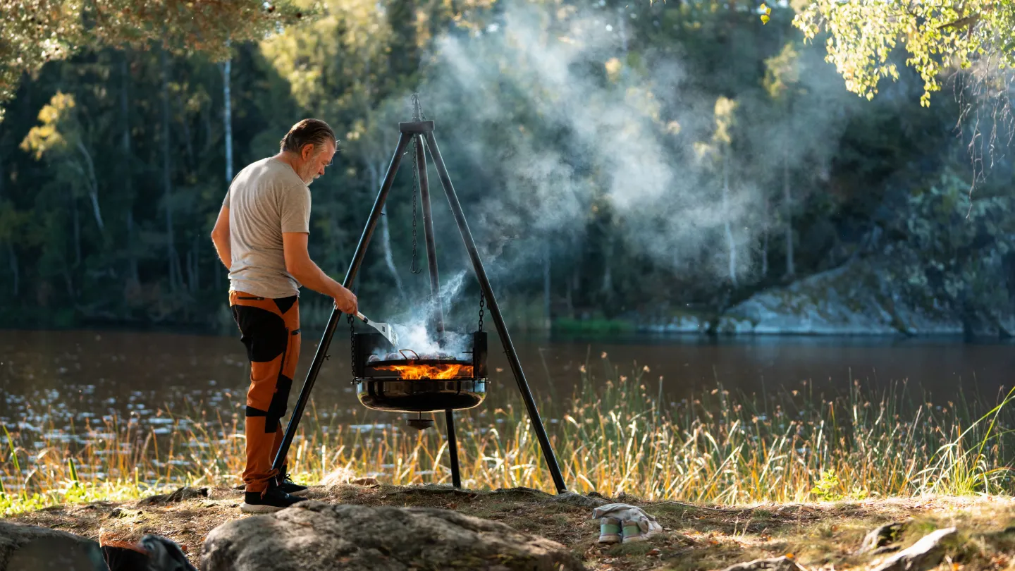 Man som grillar på en grill ute i naturen vid en sjö.